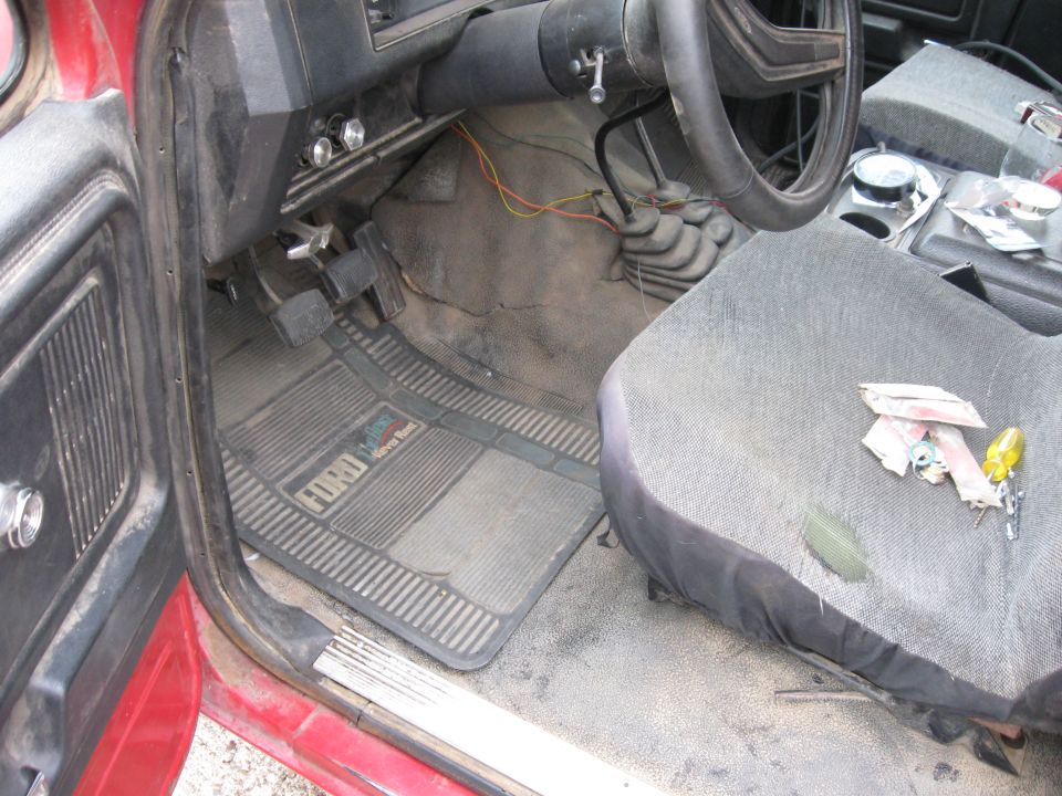 Interior of a 1981 Ford Bronco showing floor mats with Ford logo, pedals, steering wheel, and seat