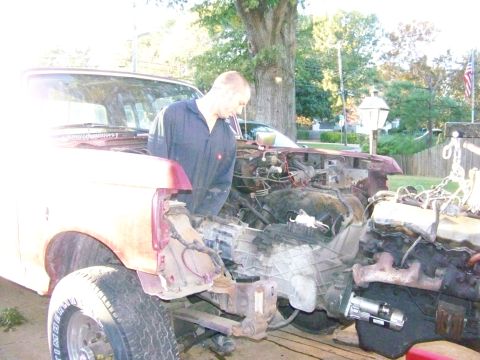 1985 Ford Bronco - The front end of a red Ford Bronco is disassembled, revealing the engine bay as a person works on it.