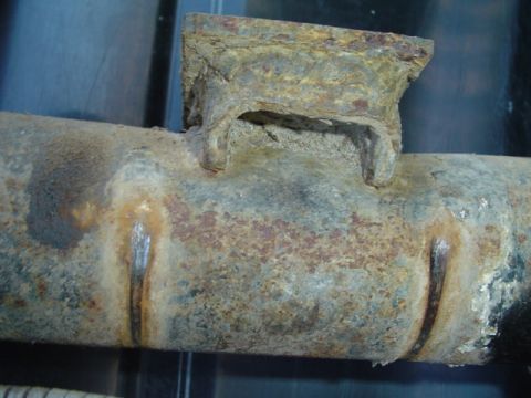 1993 Ford Bronco - Close-up of a corroded metal pipe with a bracket, likely a vehicle part, with visible rust and wear.