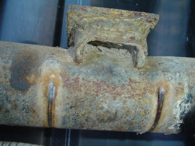 Heavily rusted metal pipe with a welded bracket, showing signs of wear and corrosion