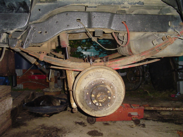 Truck rear axle on leaf springs with wheel removed showing white brake drum and lug studs
