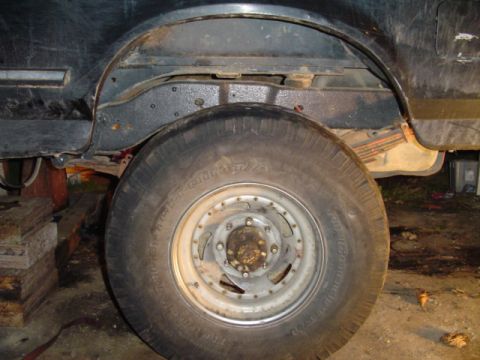 1993 Ford Bronco - The rear wheel well and suspension of a black 1993 Ford Bronco are visible, showing leaf springs and a large tire.