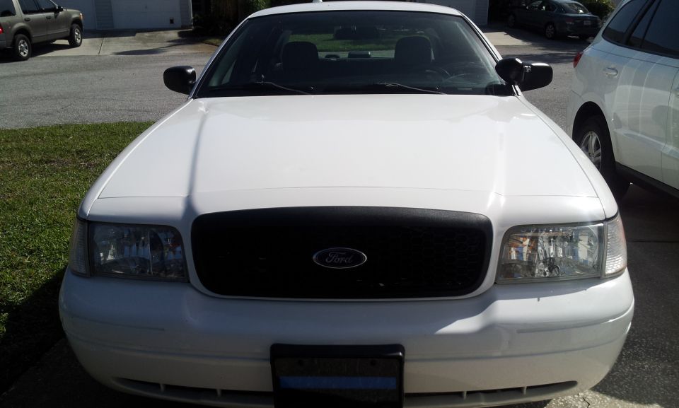 Front view of a white 2005 Ford Crown Victoria with a black grille. Another SUV and a white vehicle are parked nearby