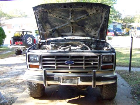 1985 Ford Bronco - Front view of a Ford truck with its hood open, revealing the engine bay. A second Ford vehicle is visible behind it.