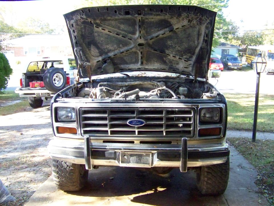 Front view of a Ford truck with hood open, showing engine. Another Ford SUV is parked behind it