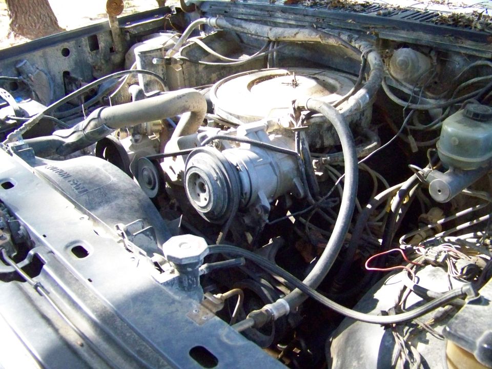 engine bay with AC compressor, radiator, and hoses visible. Some text on fan shroud