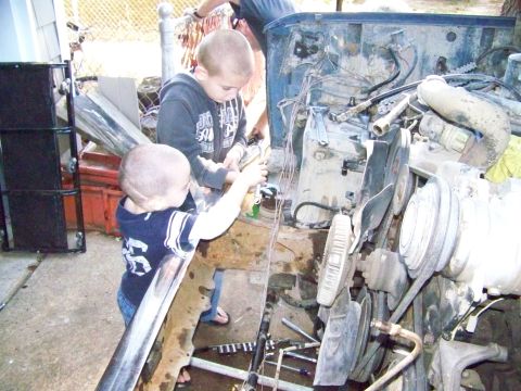 1985 Ford Bronco - Two young boys are seen working on the engine bay of a vehicle, possibly during a repair or project.