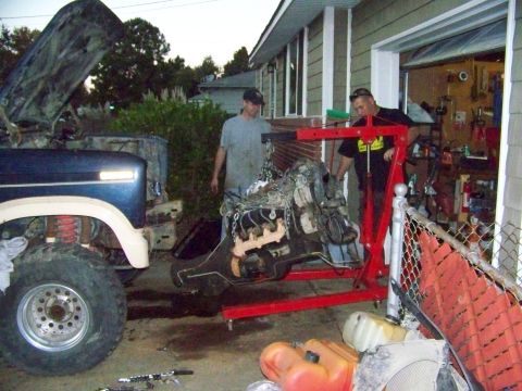 1985 Ford Bronco - Two men work on removing an engine from a Ford truck using a red engine hoist.