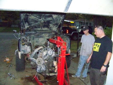 1985 Ford Bronco - Two men observe as an engine is hoisted out of a truck, likely for a swap.