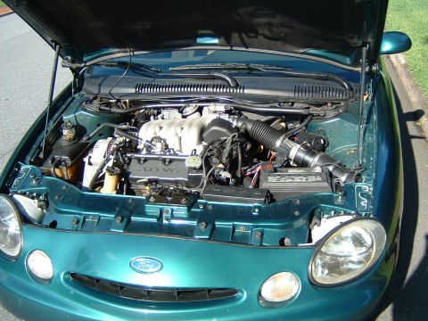 1997 Ford Taurus - The engine bay of a green 1997 Ford Taurus is visible with the hood raised.