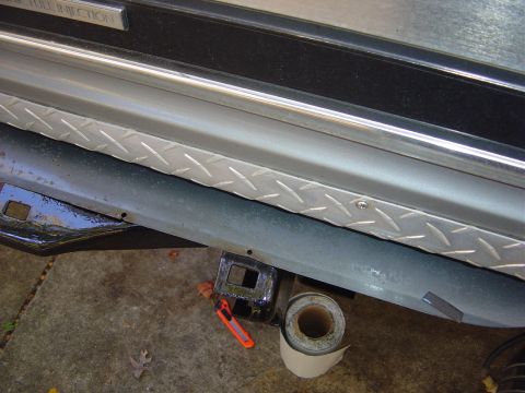 1986 Ford Bronco - The rear of a vehicle is shown, a hitch receiver and diamond plate trim, with a utility knife and tape nearby.