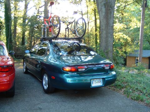 1997 Ford Taurus - Rear view of a green 1997 Ford Taurus sedan with bicycles mounted on a roof rack, parked next to a red car.