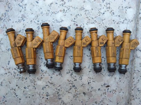 1998 Ford Crown Victoria - A set of eight yellow fuel injectors are laid out on a speckled surface.