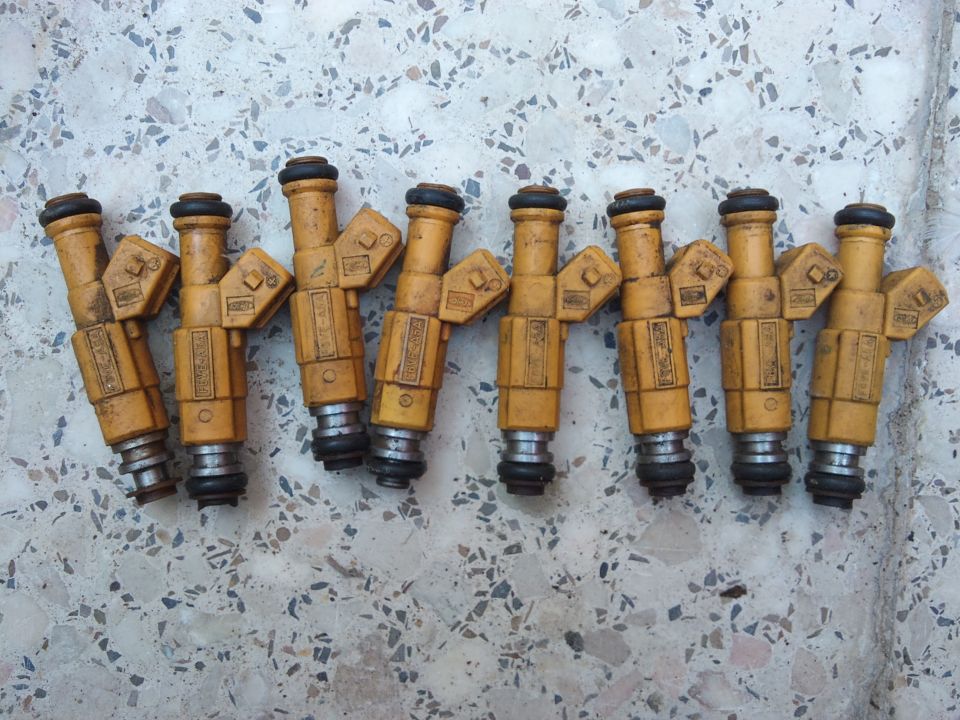 Eight yellow fuel injectors with black O-rings on a speckled surface