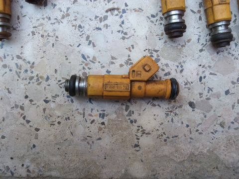 1998 Ford Crown Victoria - Close-up of yellow fuel injectors, one with visible part number 120055 701, resting on a textured surface.