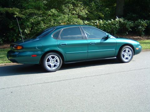 1997 Ford Taurus - A green sedan is parked on the side of a road with trees in the background.