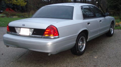 2000 Ford Crown Victoria - A silver 2000 Ford Crown Victoria is viewed from the rear, parked on a paved surface with trees in the background.