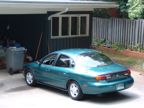 1997 Ford Taurus - A teal 1997 Ford Taurus sedan is parked outside a garage.