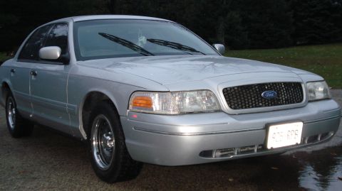 2000 Ford Crown Victoria - A silver 2000 Ford Crown Victoria is parked on a gravel surface with trees in the background.