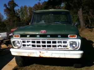 1995 Ford Bronco - This green Ford truck is parked outdoors with trees and grass in the background. The front grille and bumper show some wear.