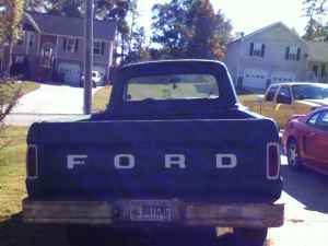 1995 Ford Bronco - Rear view of a dark blue Ford pickup truck parked outdoors with houses in the background.