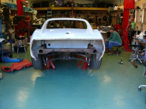1976 Chevrolet Corvette - A white Chevrolet Corvette is undergoing repairs in a workshop, viewed from the rear.