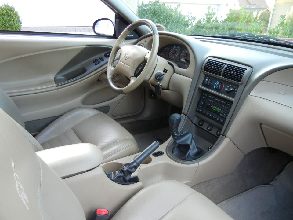 Tan leather car interior with a steering wheel, dashboard, center console, and seats visible