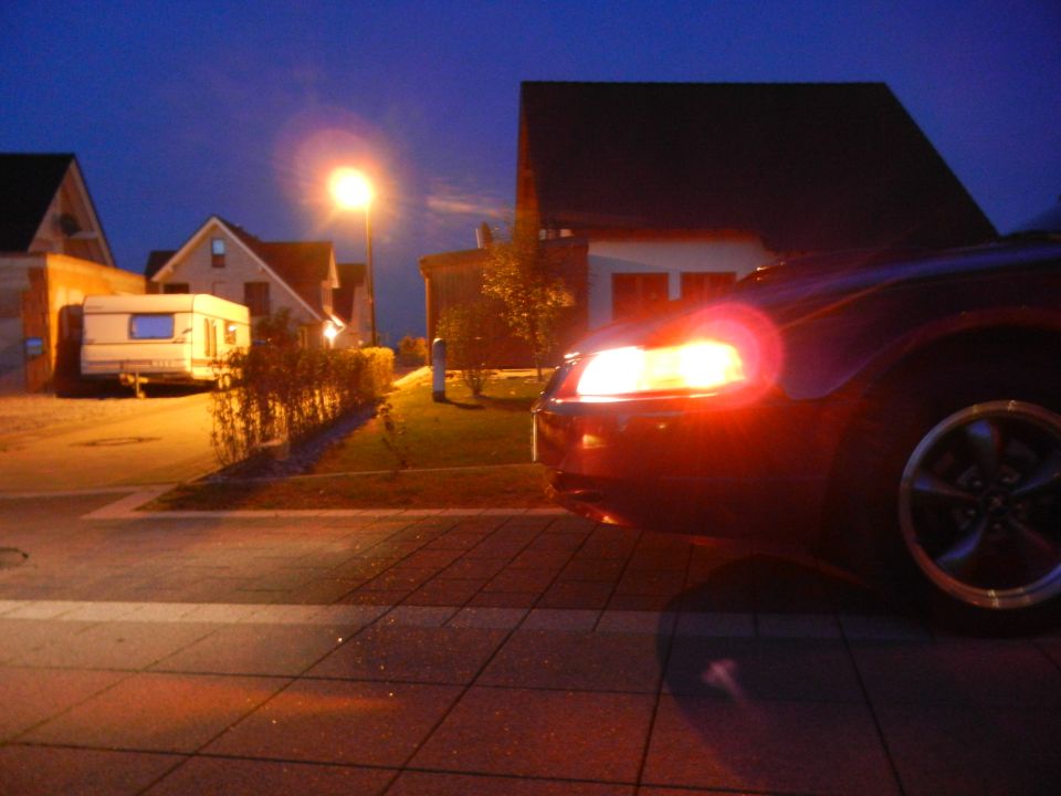 Dark sedan's front right corner with headlight on, seen at night