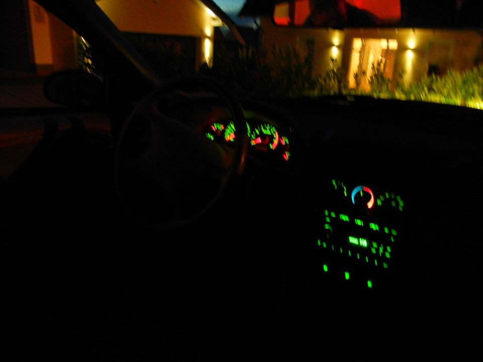 Car interior at night, dashboard lights illuminated, steering wheel and radio visible