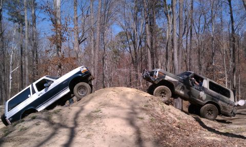 1979 Ford Bronco - Two SUVs tackle an off-road trail, demonstrating their climbing capabilities on a steep dirt incline.