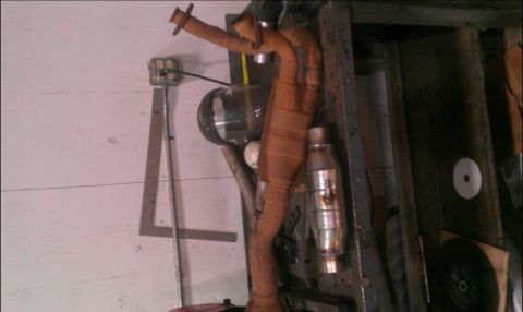 1986 Ford Bronco - A rusty exhaust manifold is shown mounted on a workbench, with various tools and parts in the background.