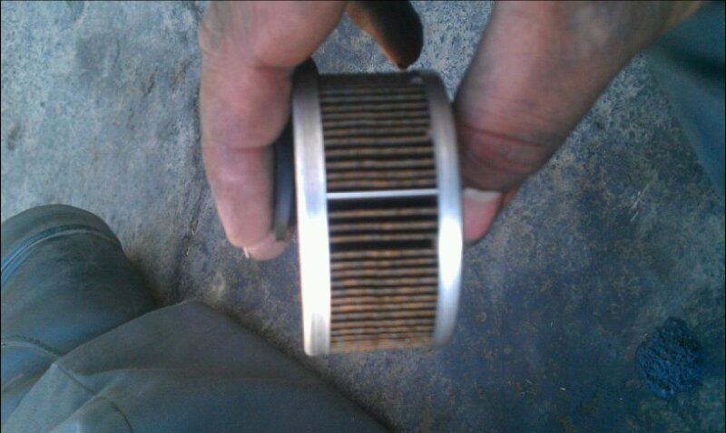 Hands holding a used oil filter with visible metal pleats