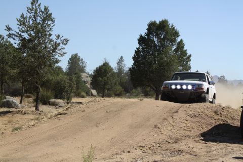 1996 Ford Bronco - A white SUV navigates a dusty off-road trail under a clear blue sky.