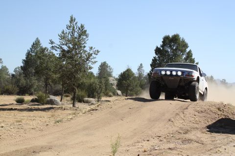 1996 Ford Bronco - An off-road SUV navigates a dusty trail in a dry, wooded landscape under a clear blue sky.