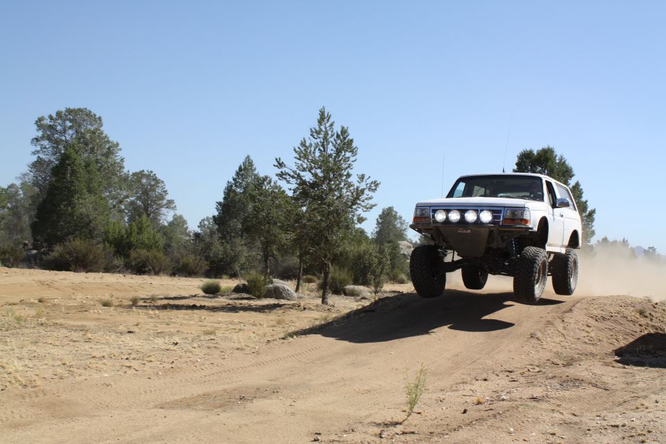 White 1996 Ford Bronco mid-air over a dirt mound, front view with four auxiliary lights
