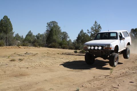 1996 Ford Bronco - White 1996 Ford Bronco mid-air jump on a dusty trail.