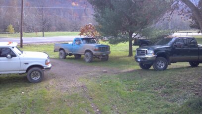 1993 Ford F-150 - Three pickup trucks are parked on a dirt lot with grass and trees in the background. The registry claims the blue truck is a 1993 Ford F-15…