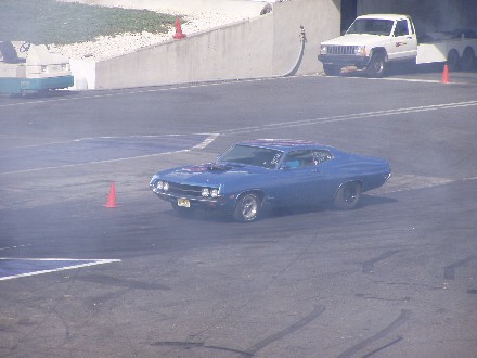 1999 Ford Crown Victoria - A blue muscle car drifts on a track, with a white Jeep Cherokee in the background.