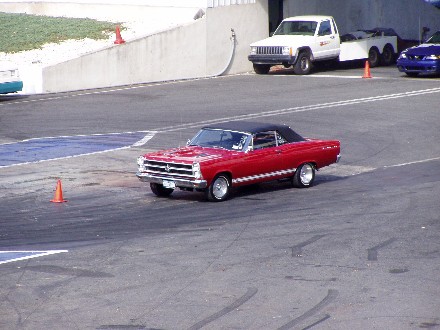 1999 Ford Crown Victoria - Red 1967 Ford Fairlane convertible driving on a race track, with other vehicles visible.