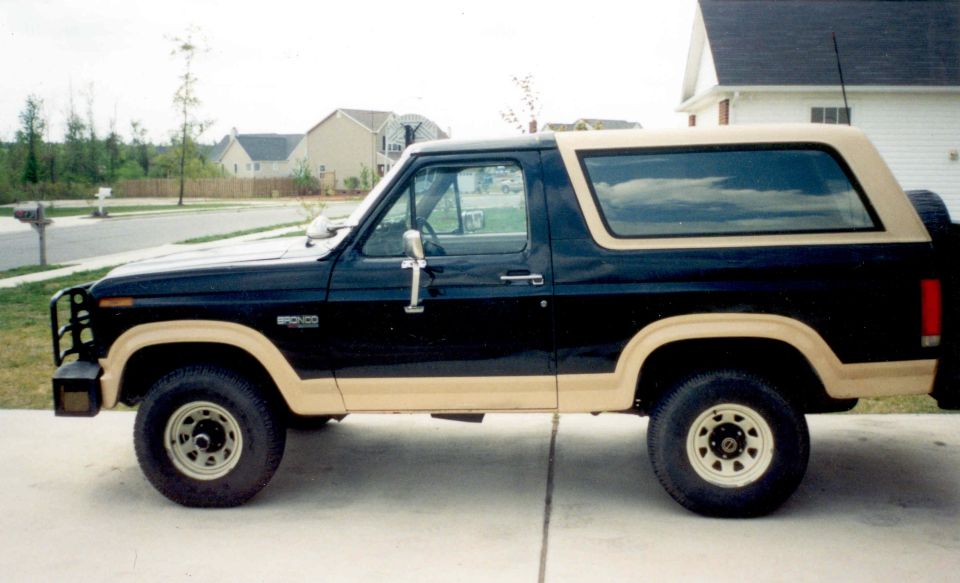 Black and tan Ford Bronco SUV, side view, lifted on white wheels in a driveway