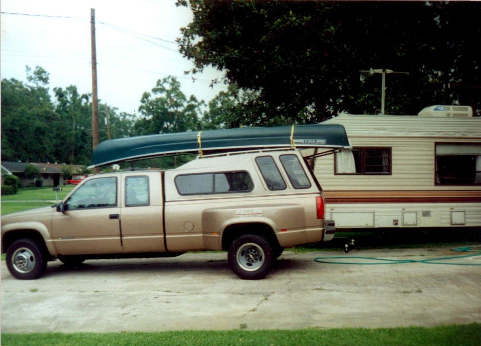 Tan Chevrolet dually pickup with canoe on cap, towing travel trailer