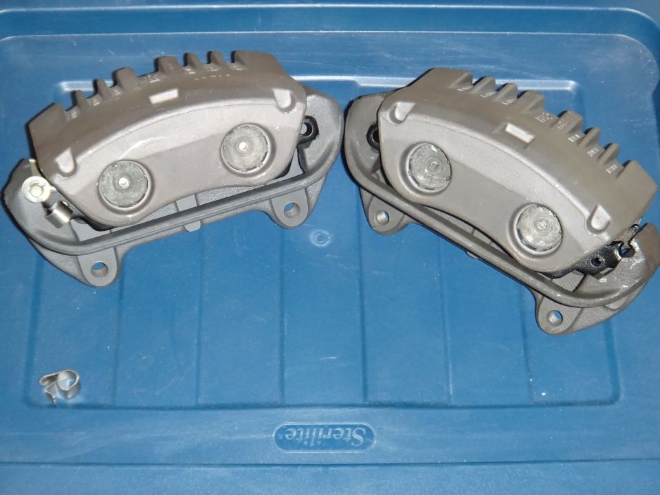 Two gray brake calipers on a blue plastic surface