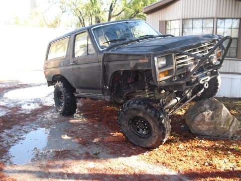 1986 Ford Bronco - Modified 1986 Ford Bronco with off-road tires and custom bumper sits on rocks and mud.