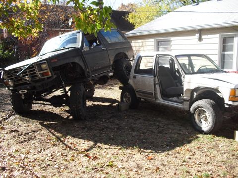 1986 Ford Bronco - Two heavily modified trucks are parked in a yard, one on top of the other.