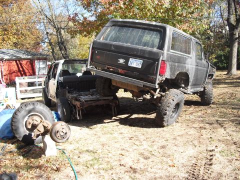 1986 Ford Bronco - A black SUV is precariously balanced atop a stripped truck chassis, with spare parts scattered nearby.