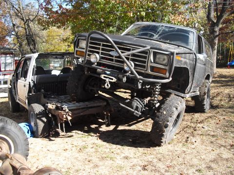 1986 Ford Bronco - A heavily modified Ford Bronco is precariously perched on top of a dismantled SUV in a yard.