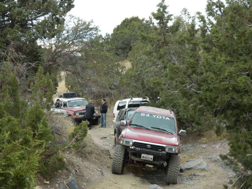Red SUV with "83 YOTA" on windshield on rocky trail with other off-road vehicles