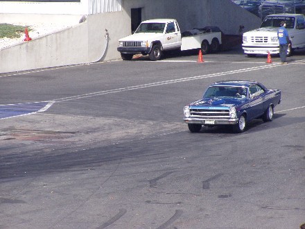 1999 Ford Crown Victoria - A blue classic car drives on a track with other vehicles in the background.