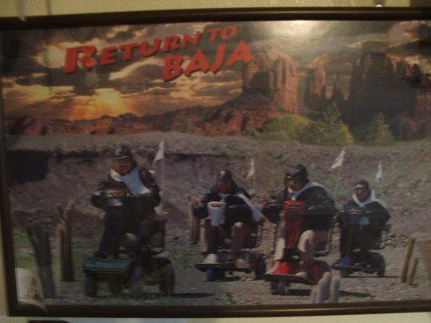Four people on mobility scooters with flags, in front of a desert landscape with "Return to Baja" text