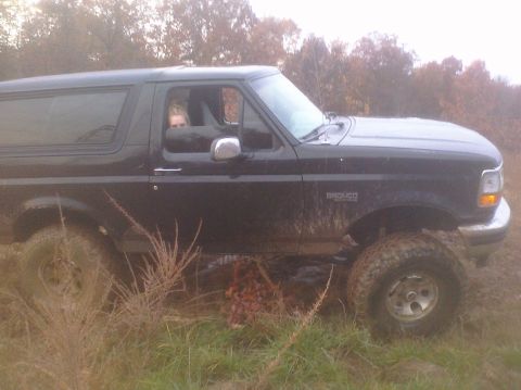 1995 Ford Bronco - Mud-covered Ford Bronco seen from the side, with a person inside, navigating rough terrain.